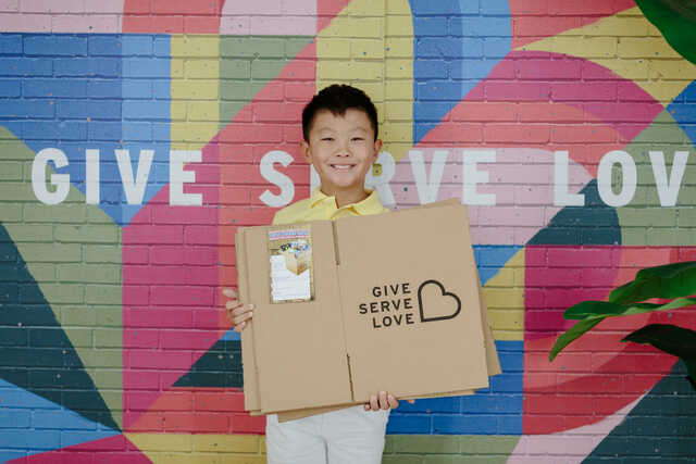 elementary school child holding snack boxes in front of the be rich mural