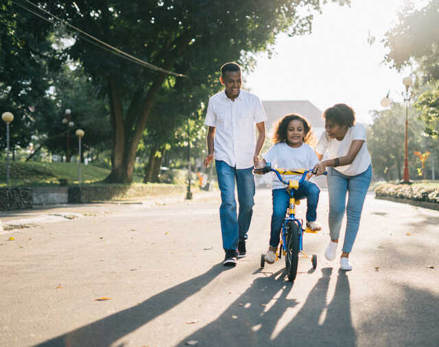 mom and dad teaching daughter to ride a bike